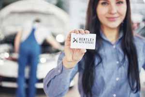 woman in a car mechanic workshop holding a Bentley Auto Repairs business card